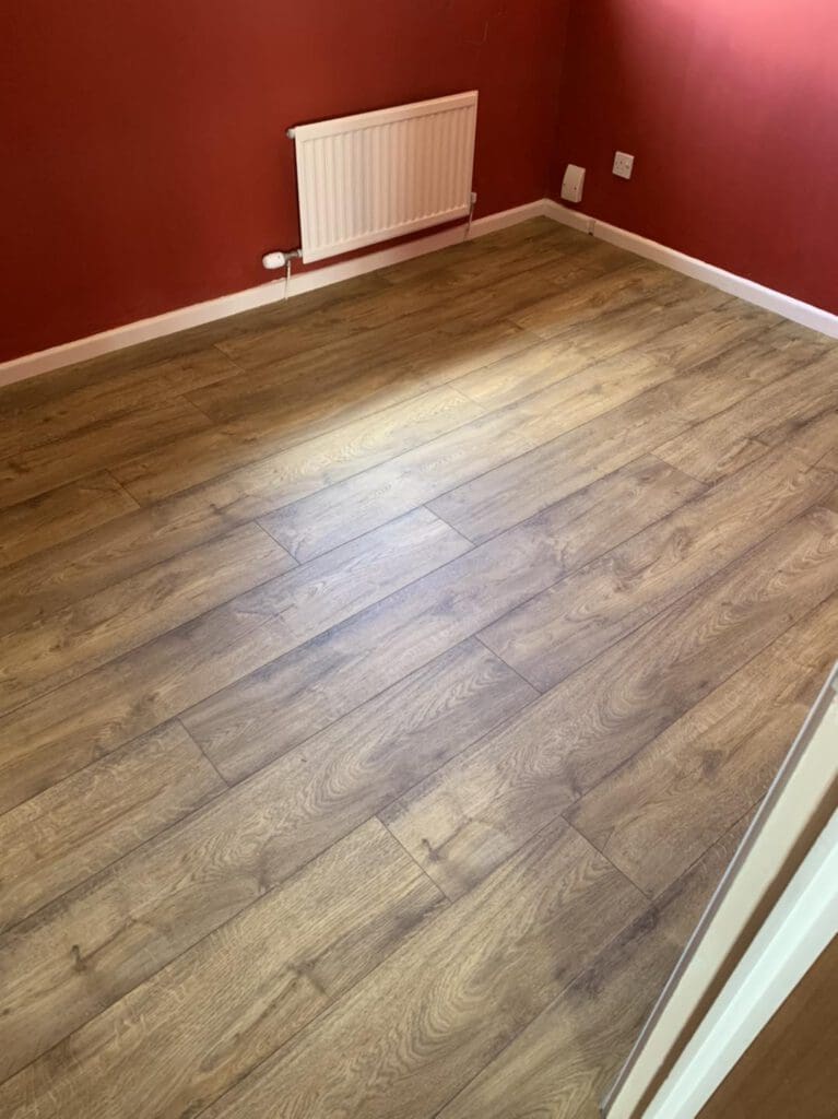A room with reddish-brown walls and light brown wood-like flooring, featuring a white wall-mounted heater.